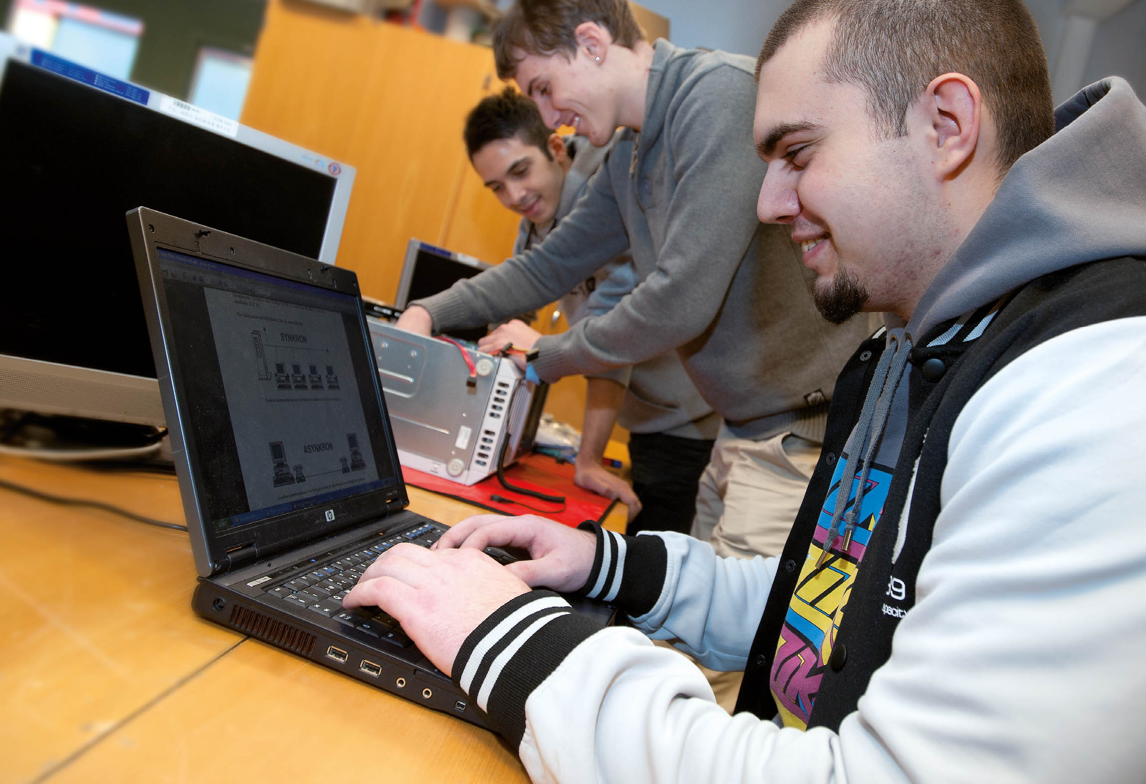 En elev använder en laptop och två elever arbetar med elektroniken i en dator