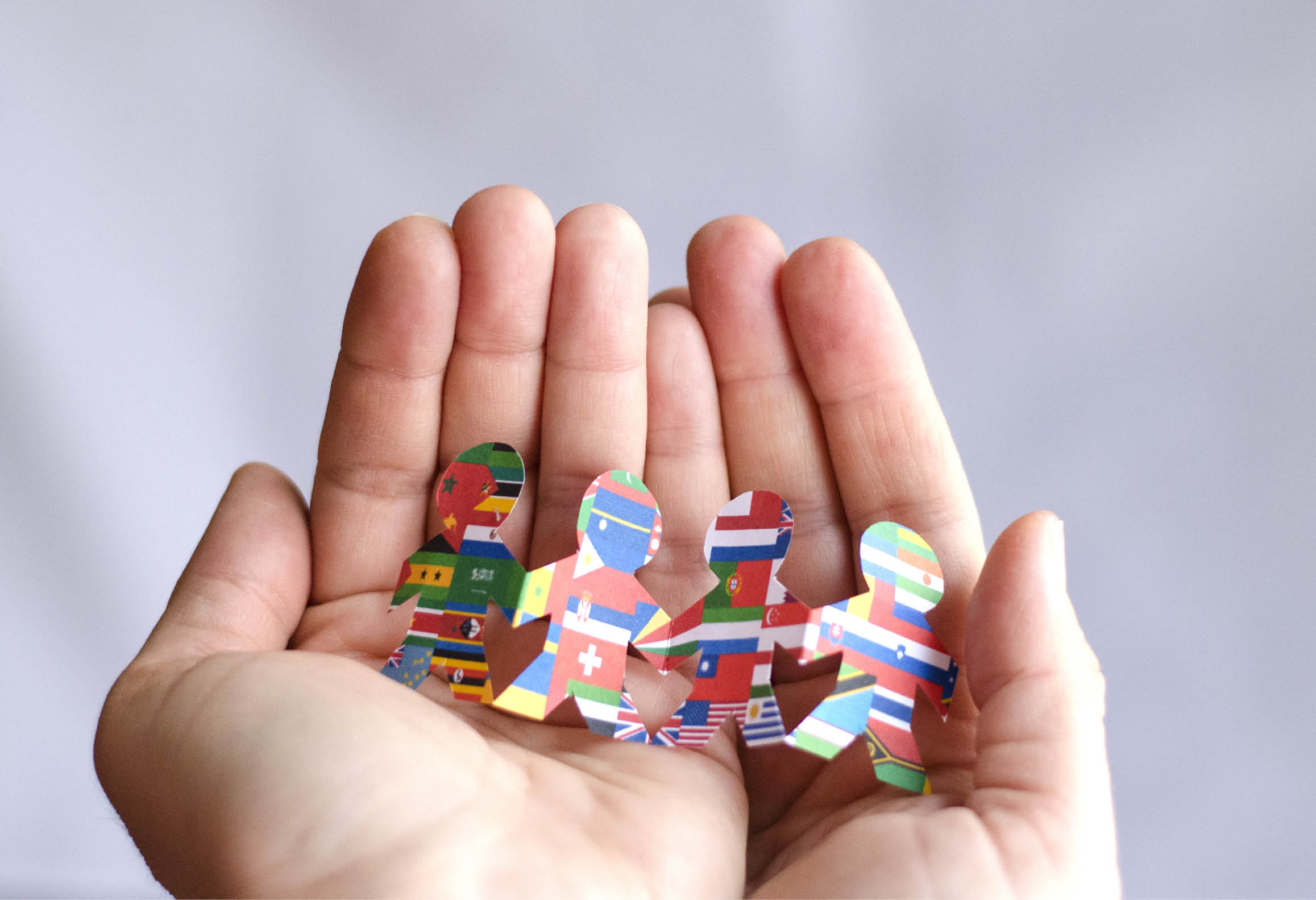 Händer som visar fram pappersfigurer med olika nationsflaggor